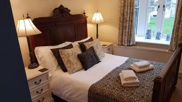 A neatly made bed with a patterned bedspread, two bedside lamps, a nightstand with drawers, and a window with curtains.