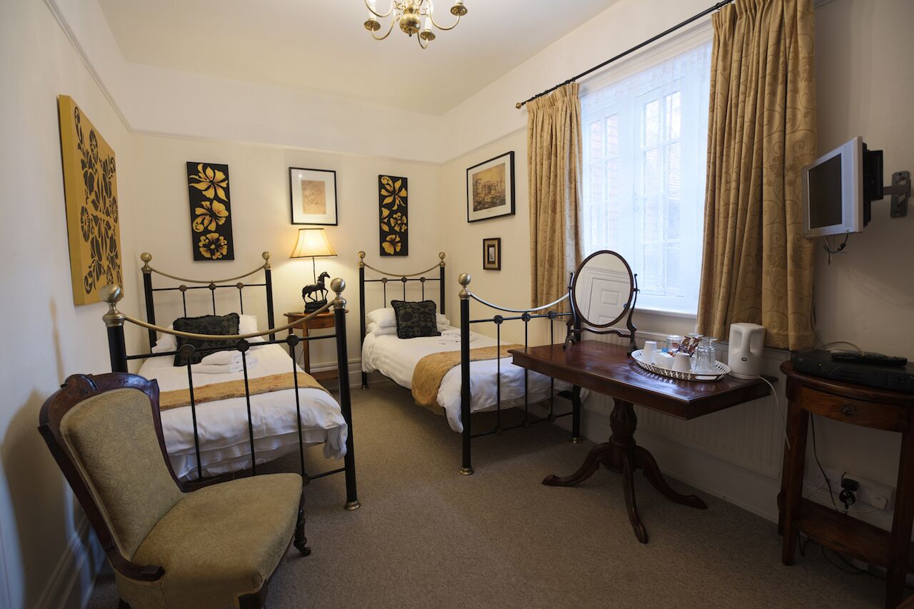 Een kamer met twee eenpersoonsbedden, een houten bureau met stoel, een televisie en kunstwerken aan de wanden.