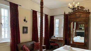 Una cama con dosel tradicional con ropa de cama blanca, un sofá de cuero con cojines rojos, un escritorio de madera con una silla y un espejo grande.