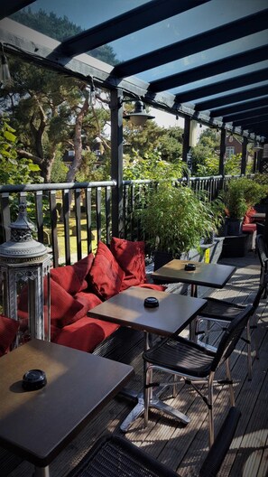 An outdoor patio with wooden tables and chairs, red cushions, and potted plants.
