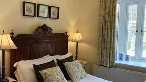 Una cama bien hecha con sábanas blancas y almohadas florales, un cabecero de madera, dos mesitas de noche con lámparas y un candelabro colgante.