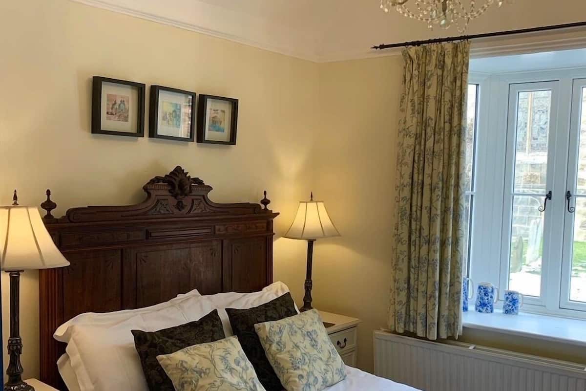 A neatly made bed with white linens and floral pillows, a wooden headboard, two bedside tables with lamps, and a chandelier above.