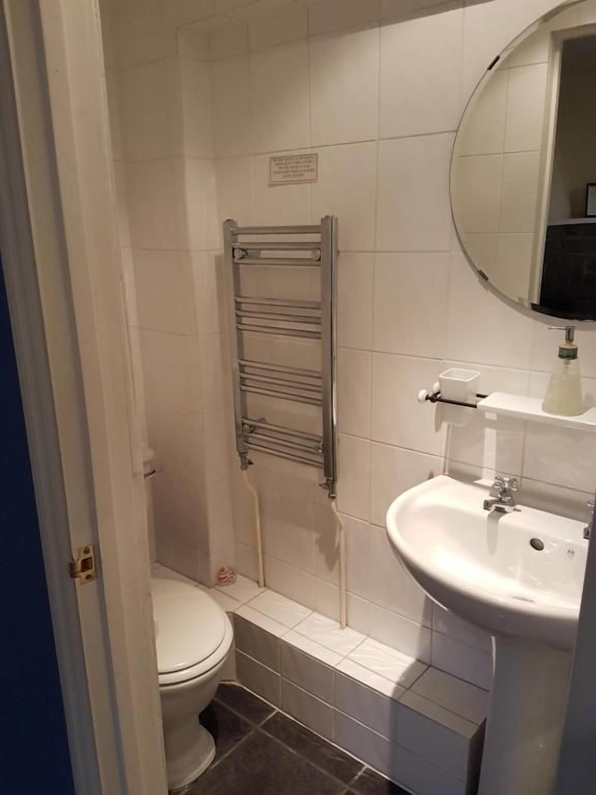 A bathroom with a toilet, a sink, a mirror, and a towel rack.