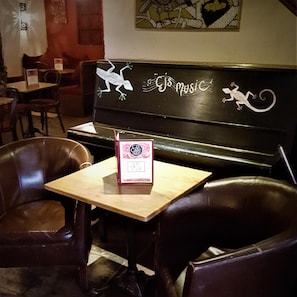 A restaurant interior with a piano, leather chairs, and a Cafe Bar sign.