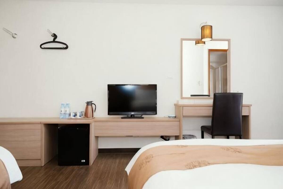 A hotel room with a bed, a desk with a television, a chair, and a mirror.