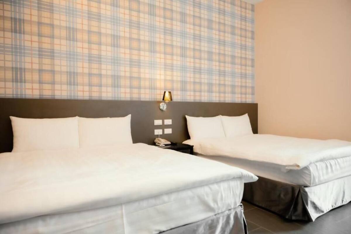 A hotel room with two beds, a headboard with a light fixture, and a plaid-patterned wall.