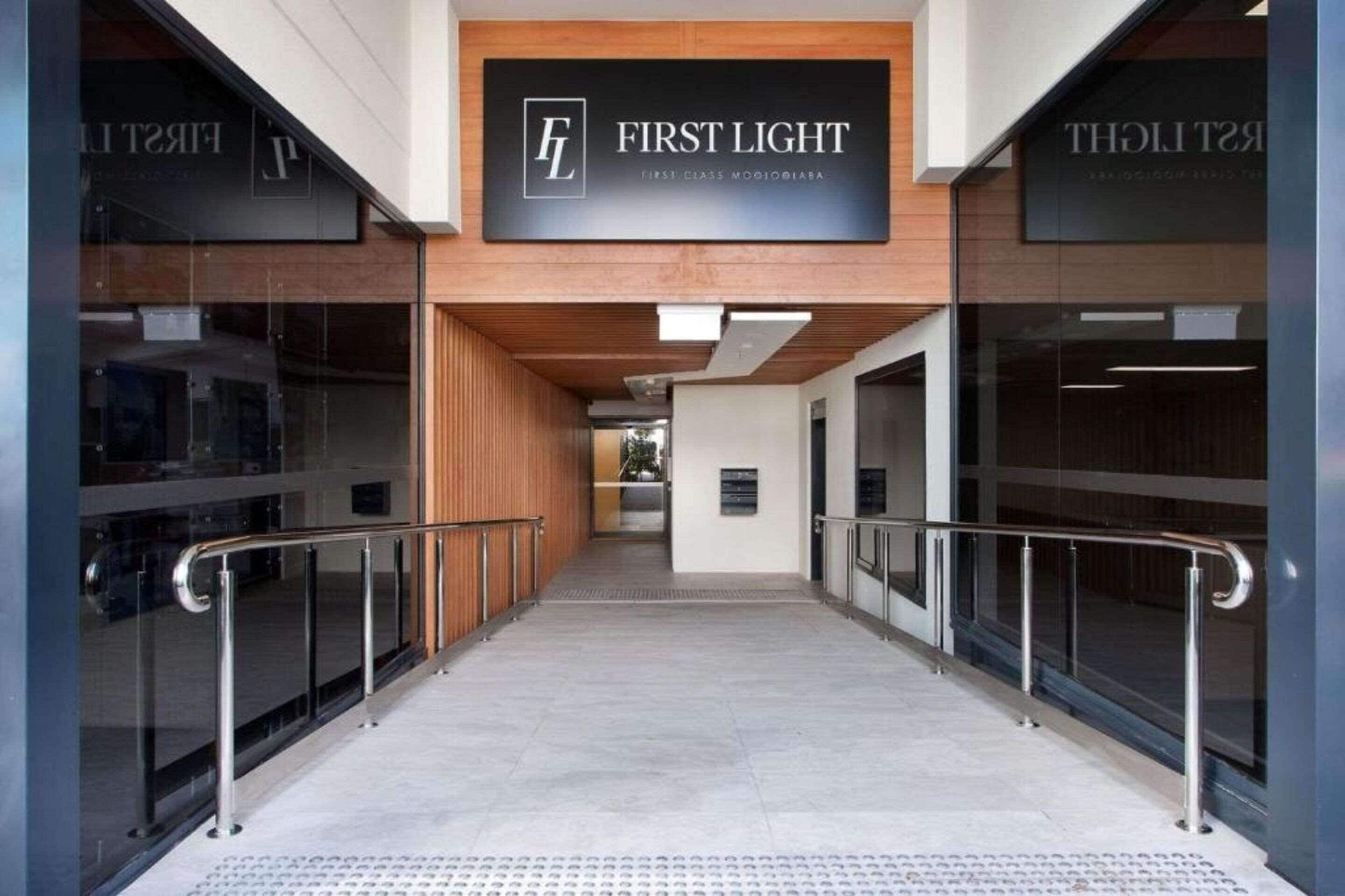 A modern hotel entrance with a sign reading "FIRST LIGHT" and "FIRST CLASS MOOIOBIABA".
