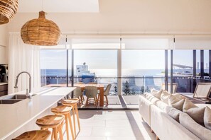 A modern kitchen with a large island, wooden stools, and a view of the sea through large windows. - First Light Mooloolaba, an Ascend Collection Hotel (Mooloolaba)