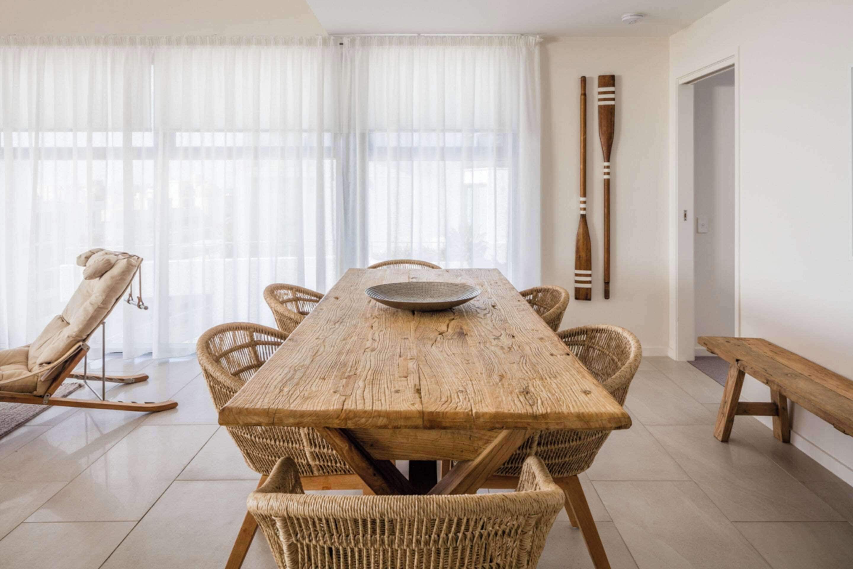 A dining area with a wooden table surrounded by wicker chairs, a bench, and two wooden paddles on the wall.