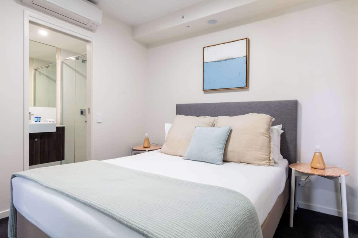A hotel room with a bed, a bedside table, a nightstand, a mirror, and a painting on the wall.