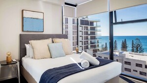 A modern hotel room with a large bed, a nightstand, and a view of the ocean through a large window. - First Light Mooloolaba, an Ascend Collection Hotel (Mooloolaba)