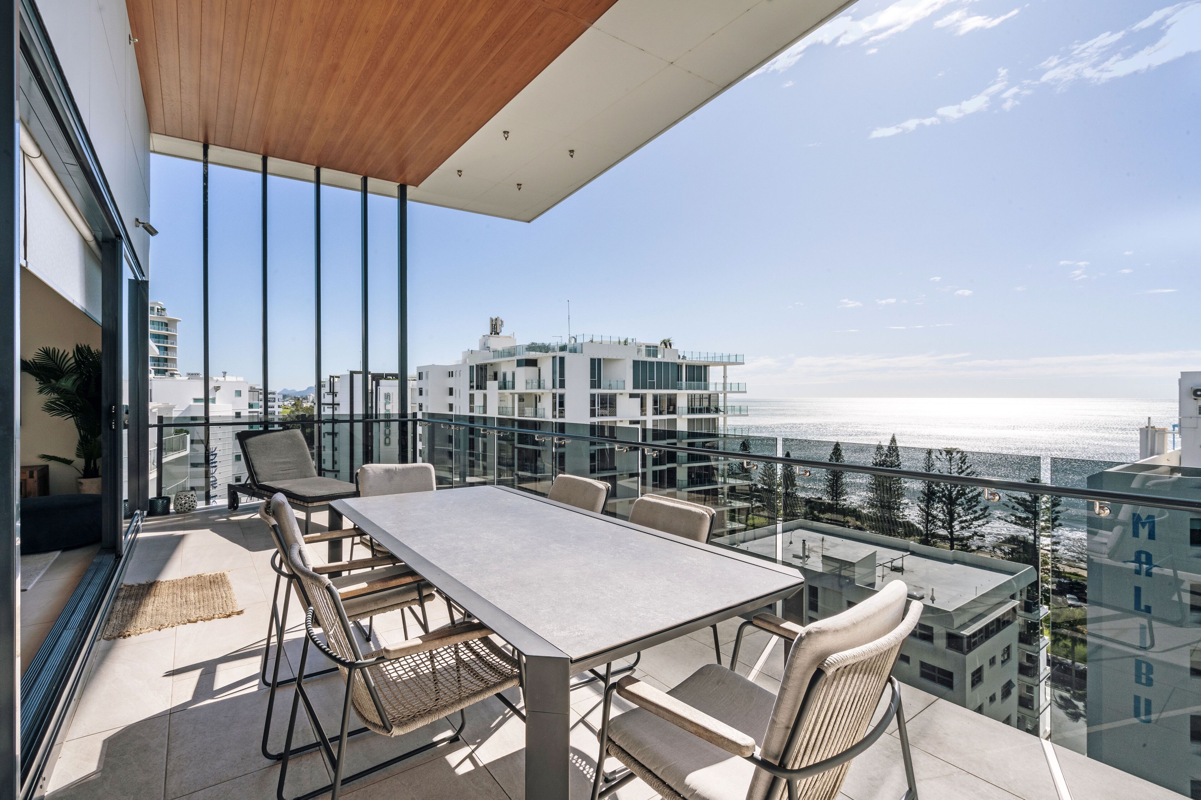 A balcony with a table and chairs, overlooking a cityscape and the sea.