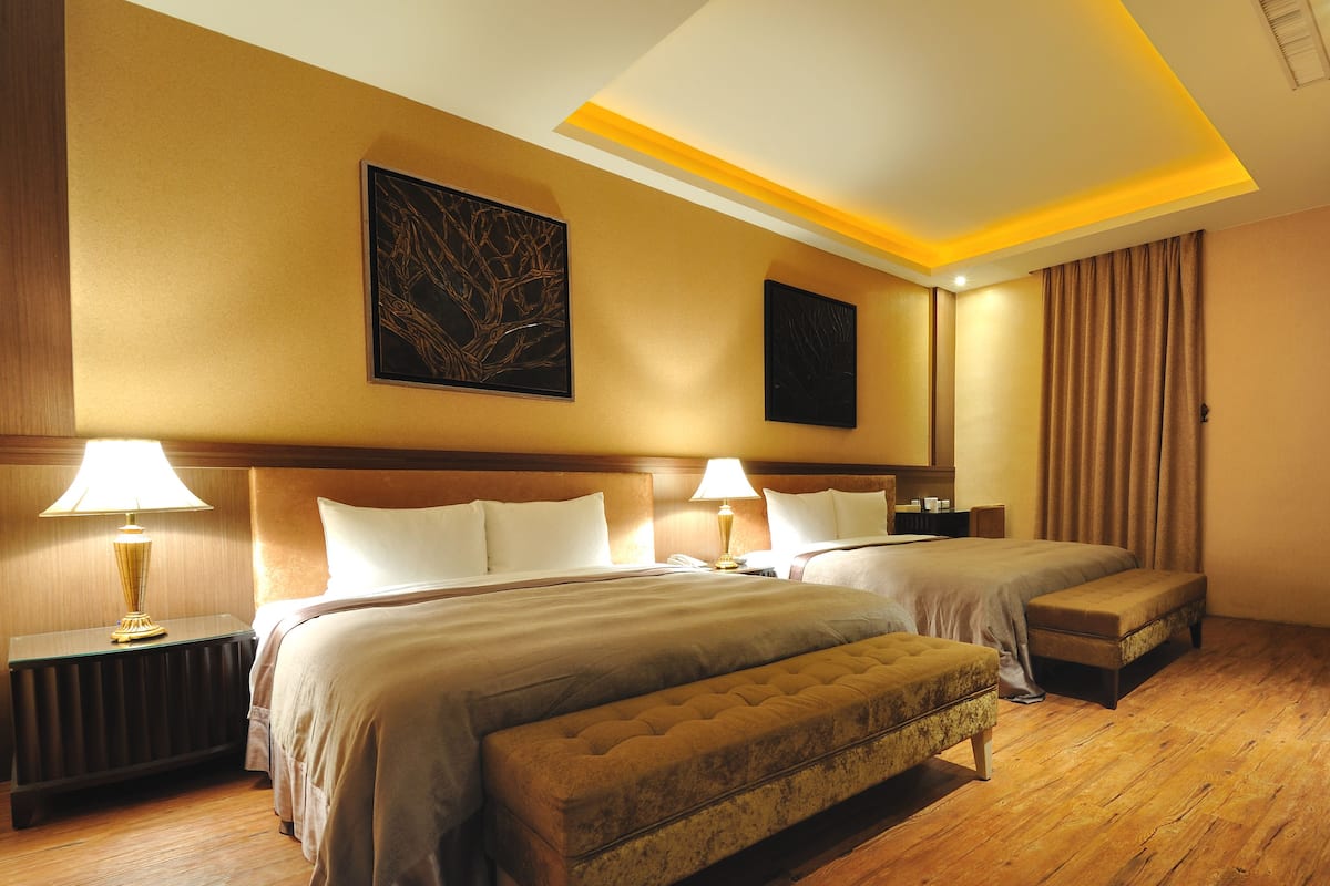Habitación de hotel con dos camas, un banco, un escritorio y una televisión.