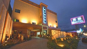 Un hotel con un llamativo letrero de neón, una entrada bien iluminada y un jardín ajardinado.