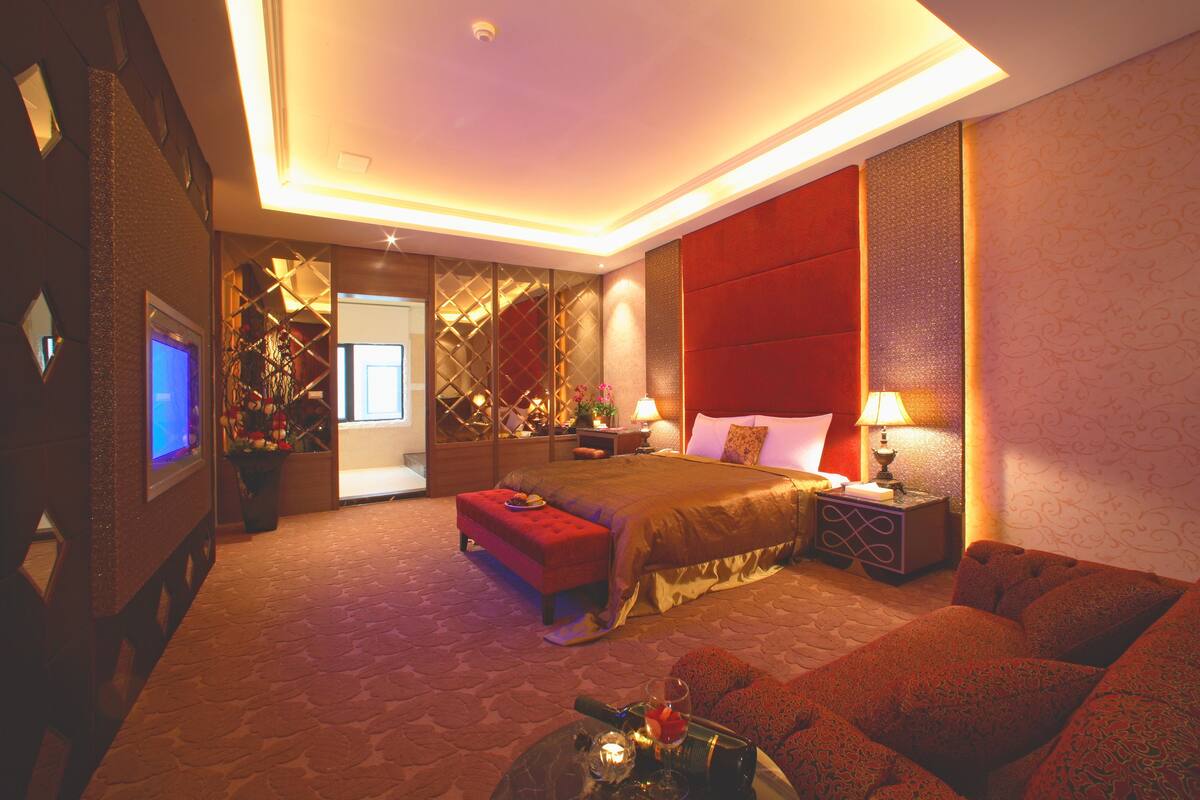 Una habitación de hotel con una cama grande, un sofá, un televisor y un escritorio con lámpara.