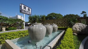 Una fuente con grandes urnas, un letrero de motel y un sendero bordeado por setos.