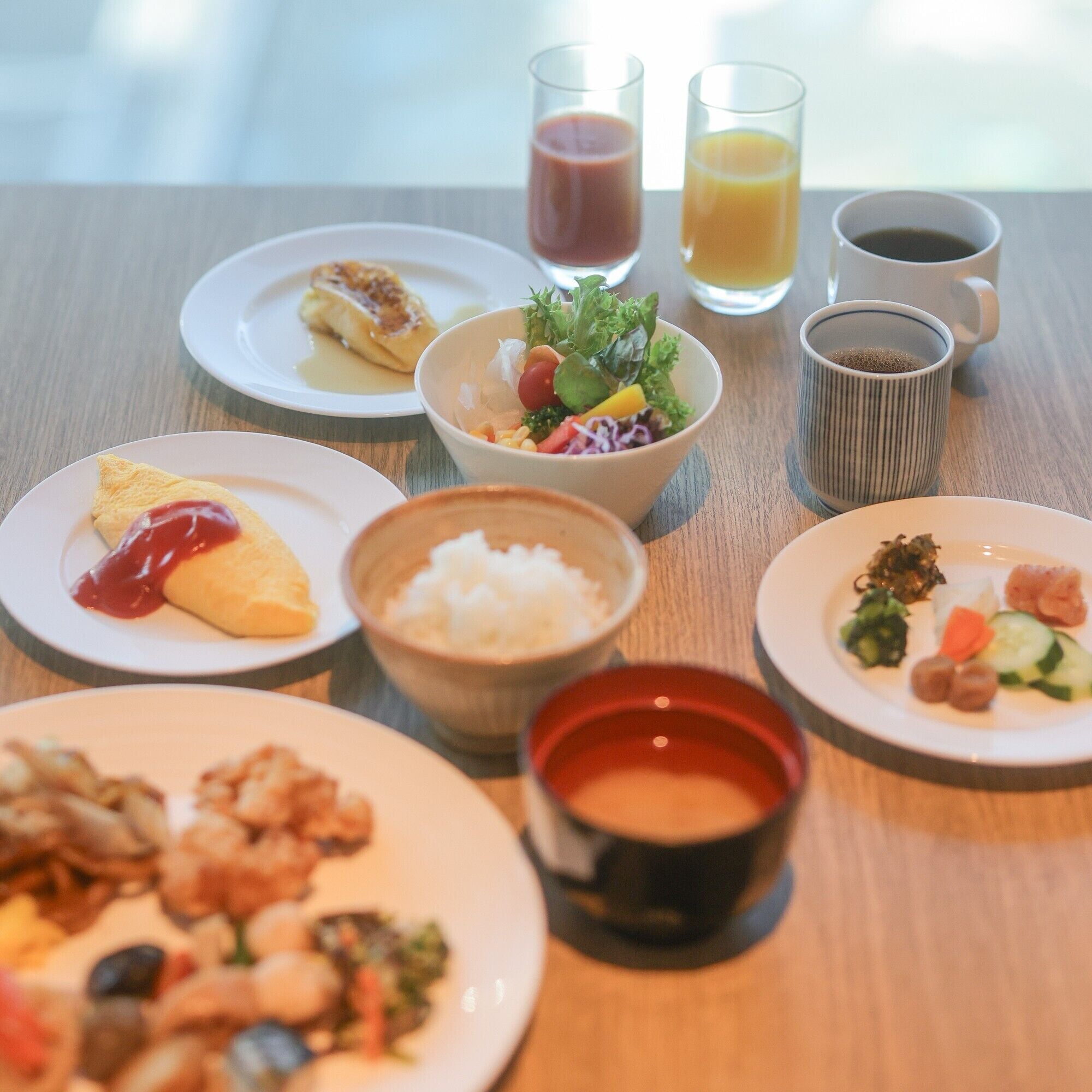 Una mesa con diversos platos, entre ellos una ensalada, arroz y un plato con verduras. También hay dos vasos de jugo y una taza de café.