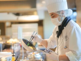 Um chef com uniforme e chapéu branco preparando comida com pauzinhos.