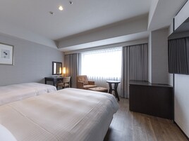 Quarto de hotel com duas camas, uma escrivaninha, uma cadeira, uma mesinha e uma televisão.