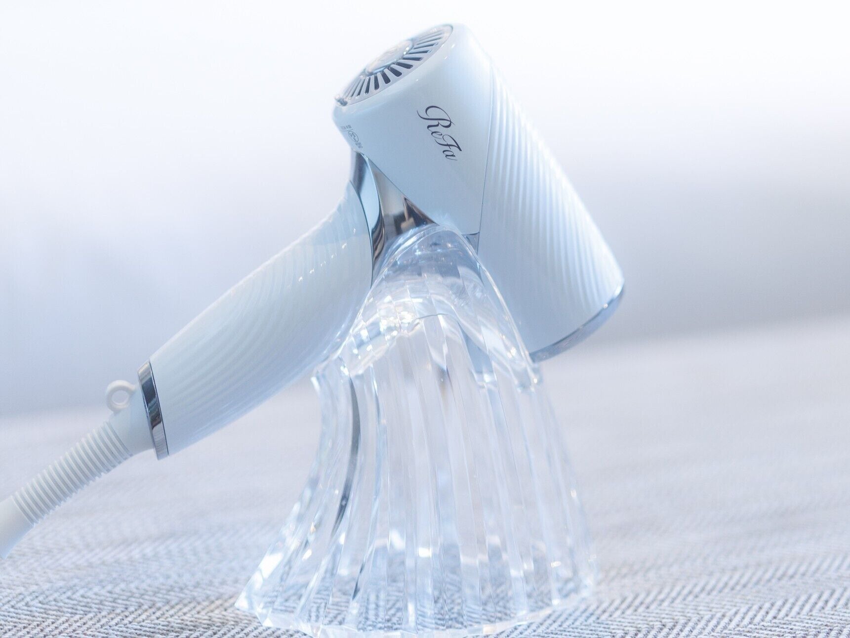 A hair dryer with a clear, ribbed handle and a transparent base.