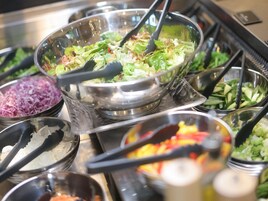 Un bufé con diversos alimentos, incluyendo ensaladas, vegetales rallados y un tazón de vegetales mixtos.