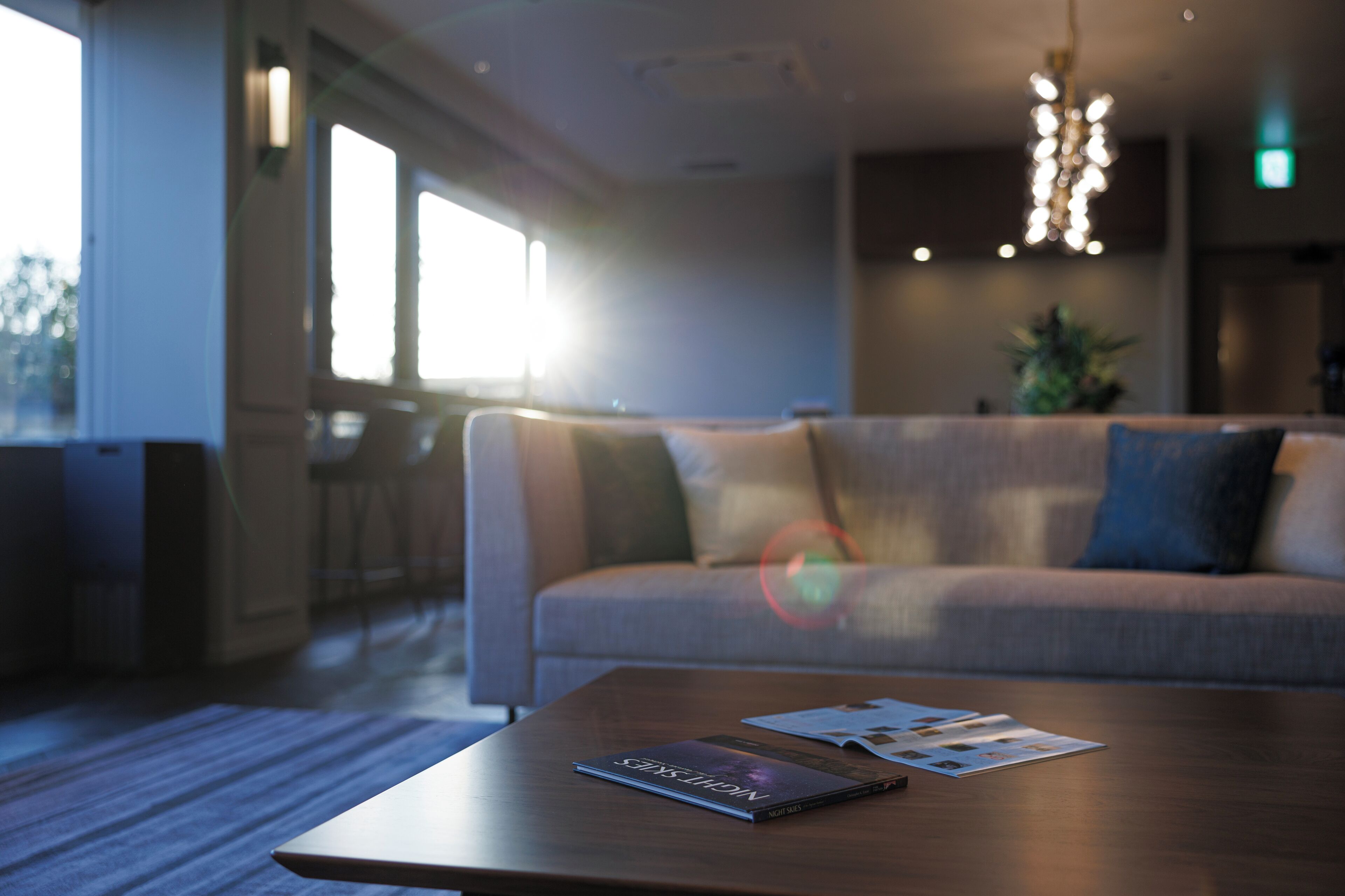 A modern hotel lobby with a sofa, a wooden coffee table with magazines, and a hanging light fixture.