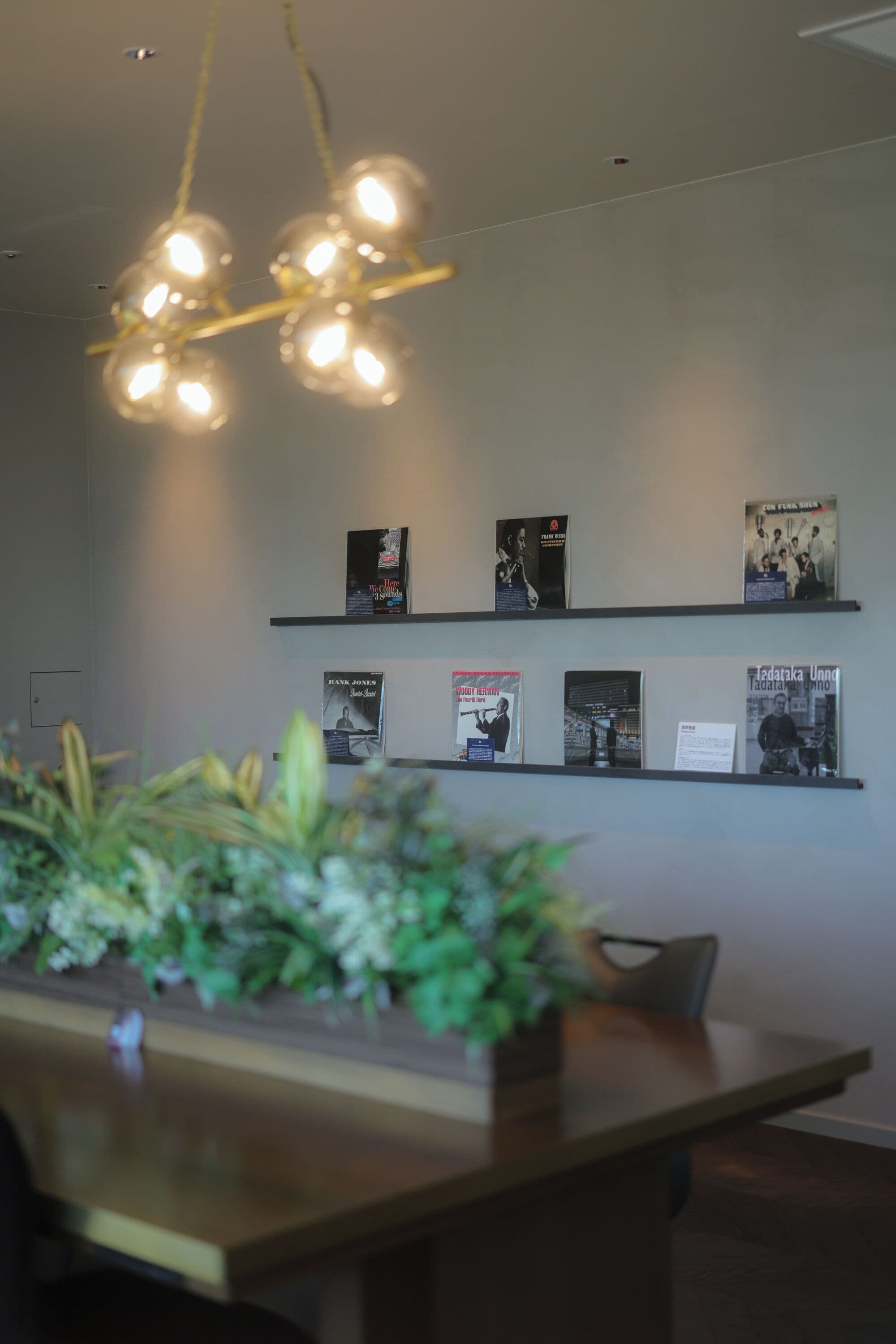 A modern interior with a wooden table, hanging lights, and wall-mounted book displays.
