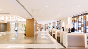 Un moderno vestíbulo de hotel con mostrador de recepción, zona de estar y una planta grande en maceta.