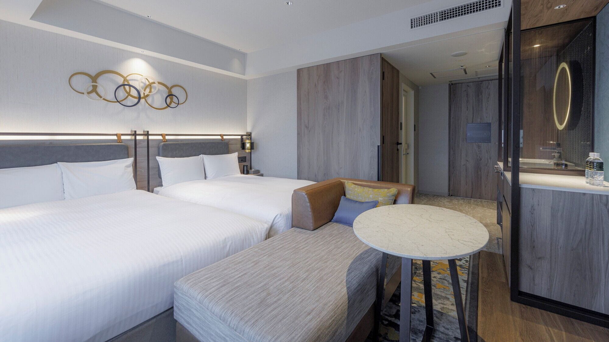 Une chambre d’hôtel avec deux lits, un coin salon, une petite table ronde et un miroir.