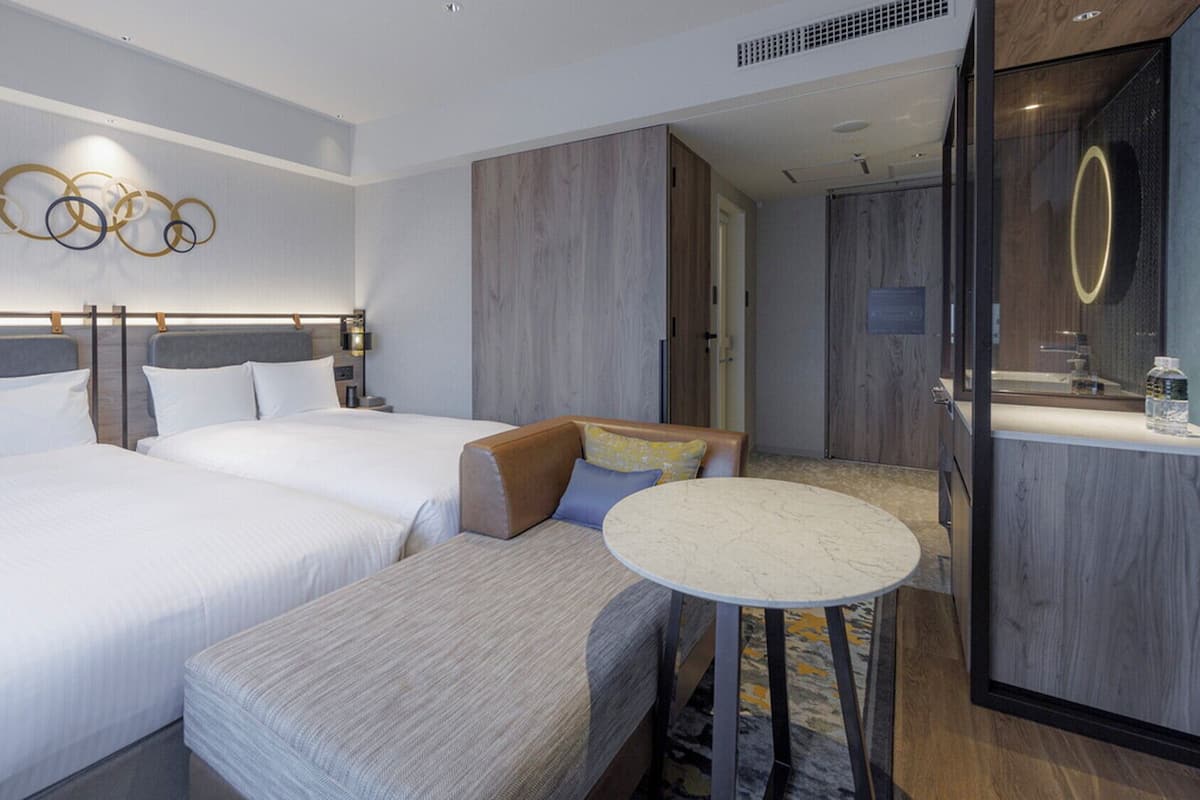Une chambre d’hôtel avec deux lits, un coin salon, une petite table ronde et un miroir.