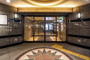 La entrada al Hotel Station Kokura de JR Kyushu, con un diseño moderno, que presenta un acceso por puerta de cristal y un patrón decorativo en el suelo.