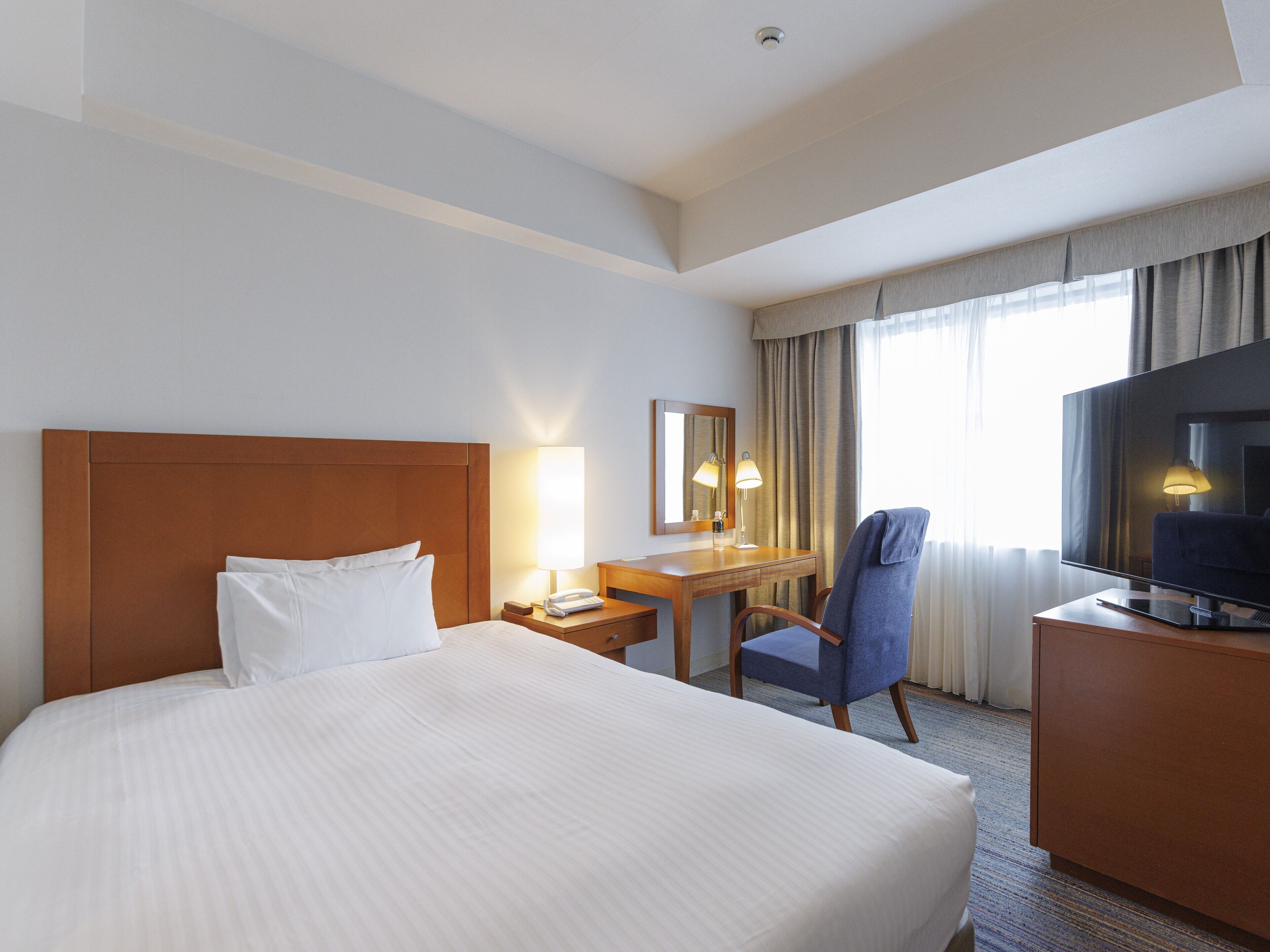 A hotel room with a large bed, a desk with a chair, a TV, and a window with curtains.
