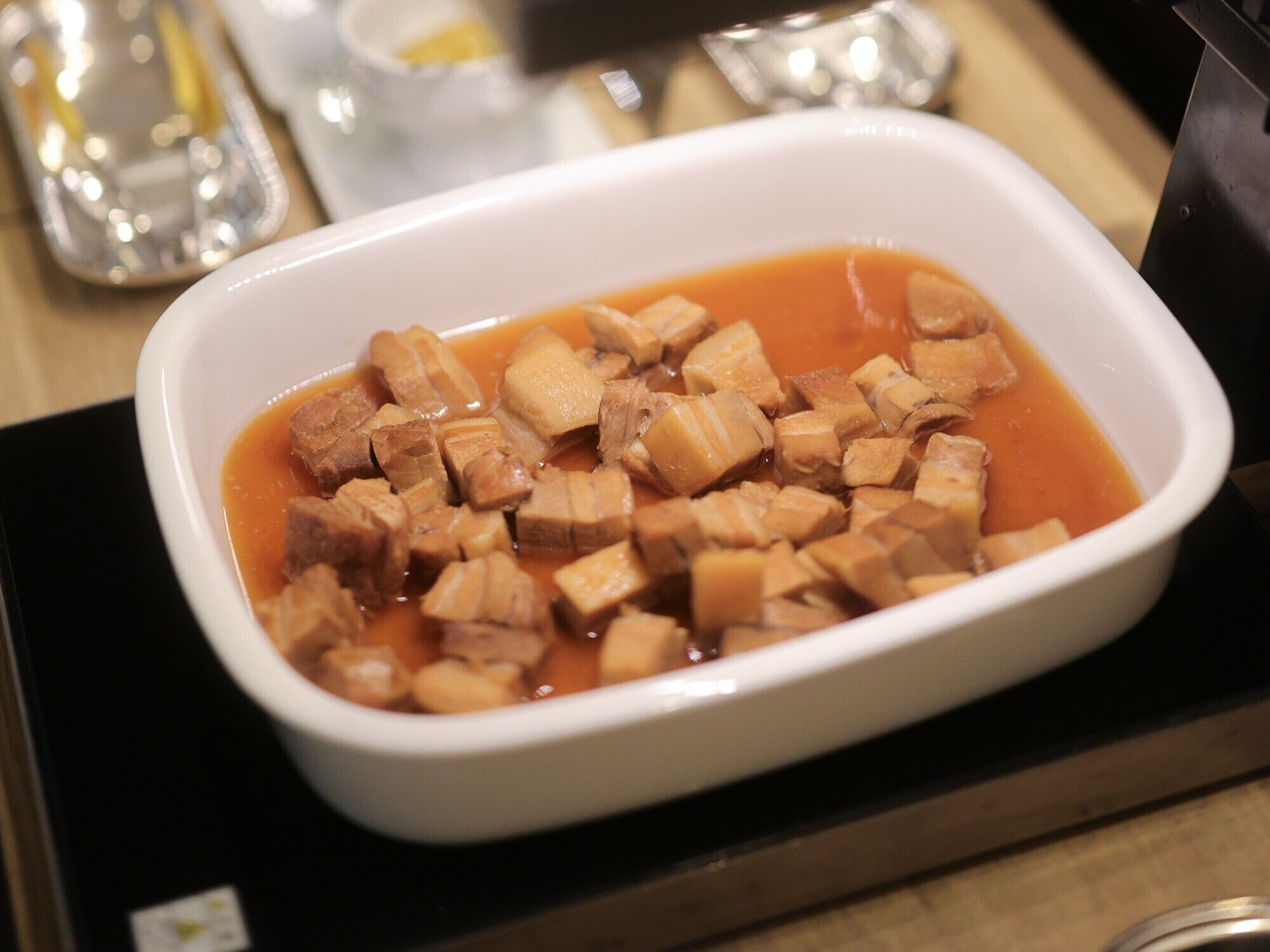 Eine weiße Schüssel mit gewürfeltem Tofu in roter Soße, auf einem schwarzen Tablett platziert.
