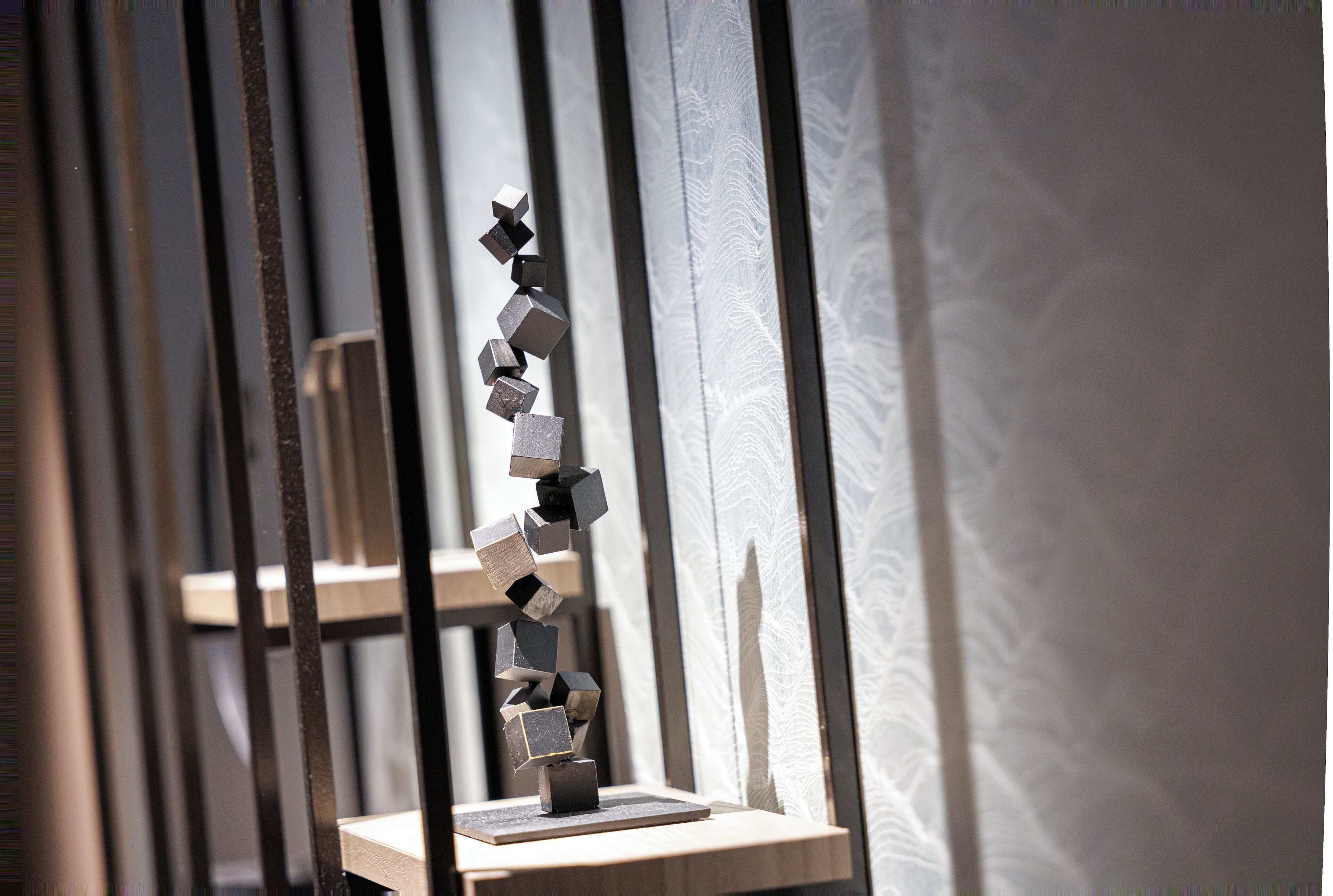 A geometric sculpture on a platform, set against a patterned wall.