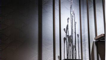 A sculpture with abstract forms on a pedestal against a textured wall.