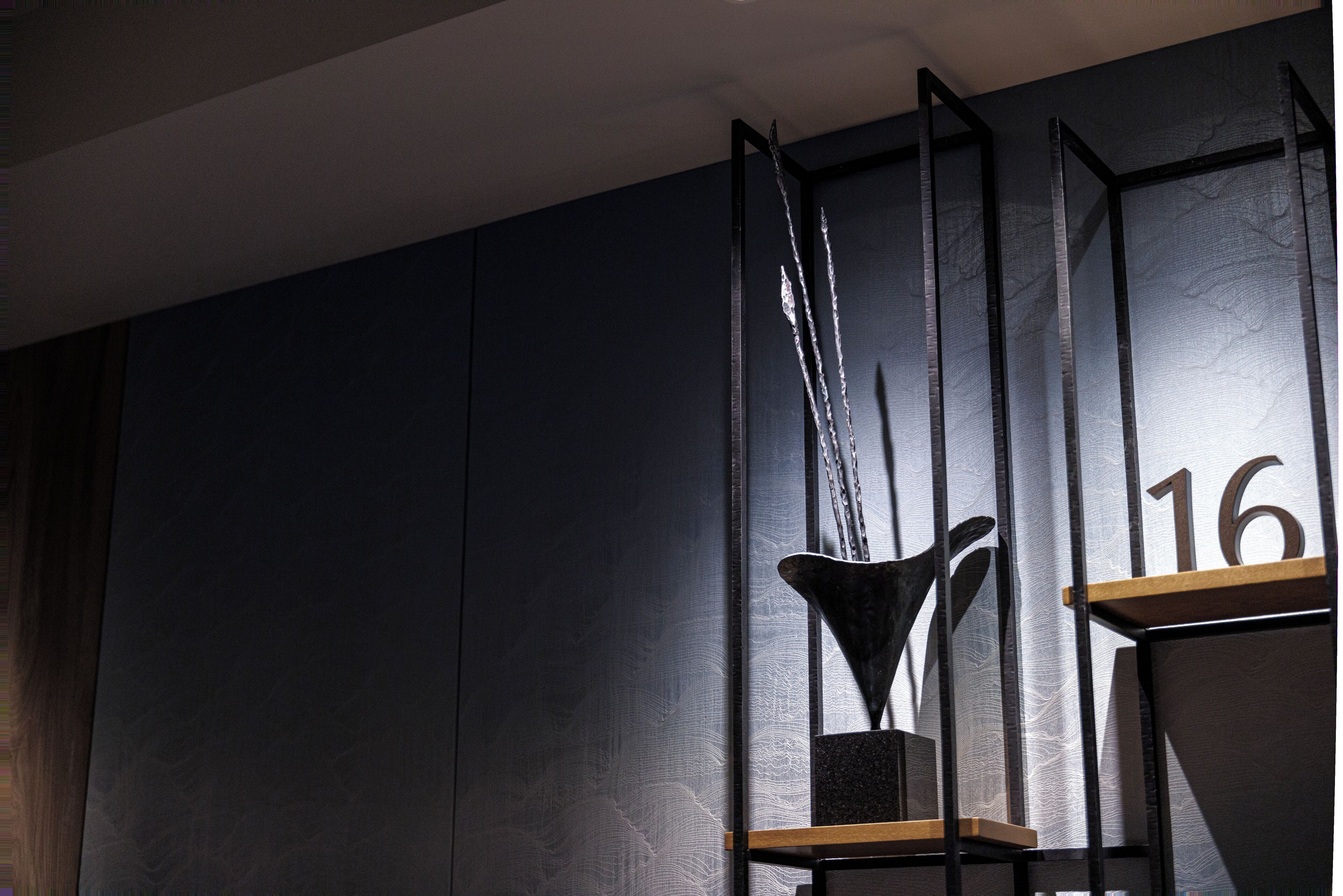 Un intérieur moderne avec un mur foncé, une étagère en métal portant le numéro « 16 », et un élément décoratif en métal.