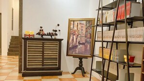A hallway with a checkered floor, a wooden cabinet with decorative items, a painting of a canal scene, and a metal bookshelf with books. - The Awesome Manor (Ji'an)