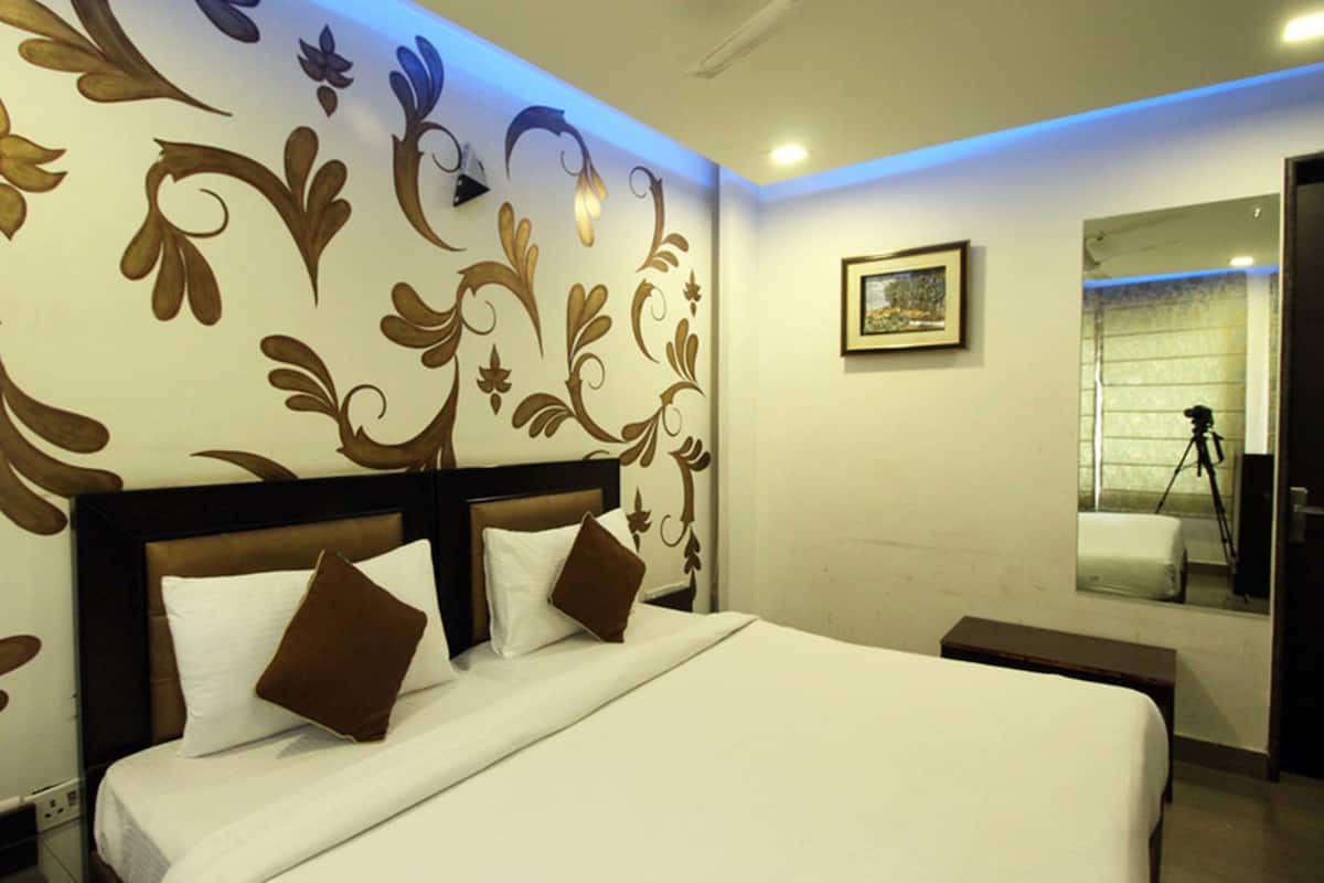 Quarto de hotel com uma cama grande, cabeceira com acabamento escuro e parede com estampas florais.