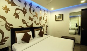 A hotel room with a large bed, a headboard with a dark finish, and a wall with floral patterns.