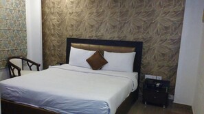 A neatly made bed with white linens and a brown pillow, a wooden nightstand with a phone and a bottle, and a patterned wallpaper on the walls.