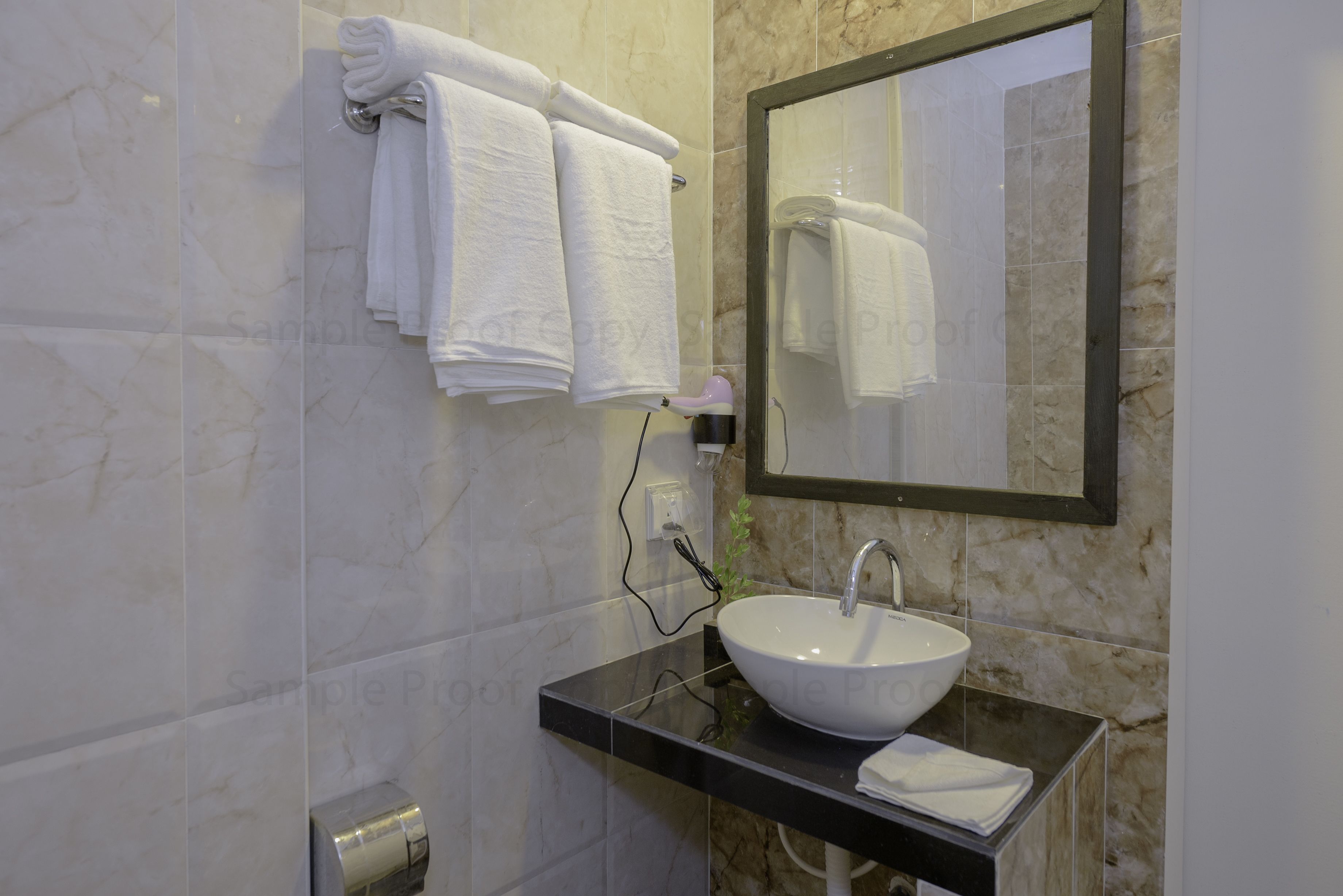 Un bagno con una parete in marmo, un piano di lavoro nero, un lavandino bianco, uno specchio e un portaservizi con asciugamani piegati.