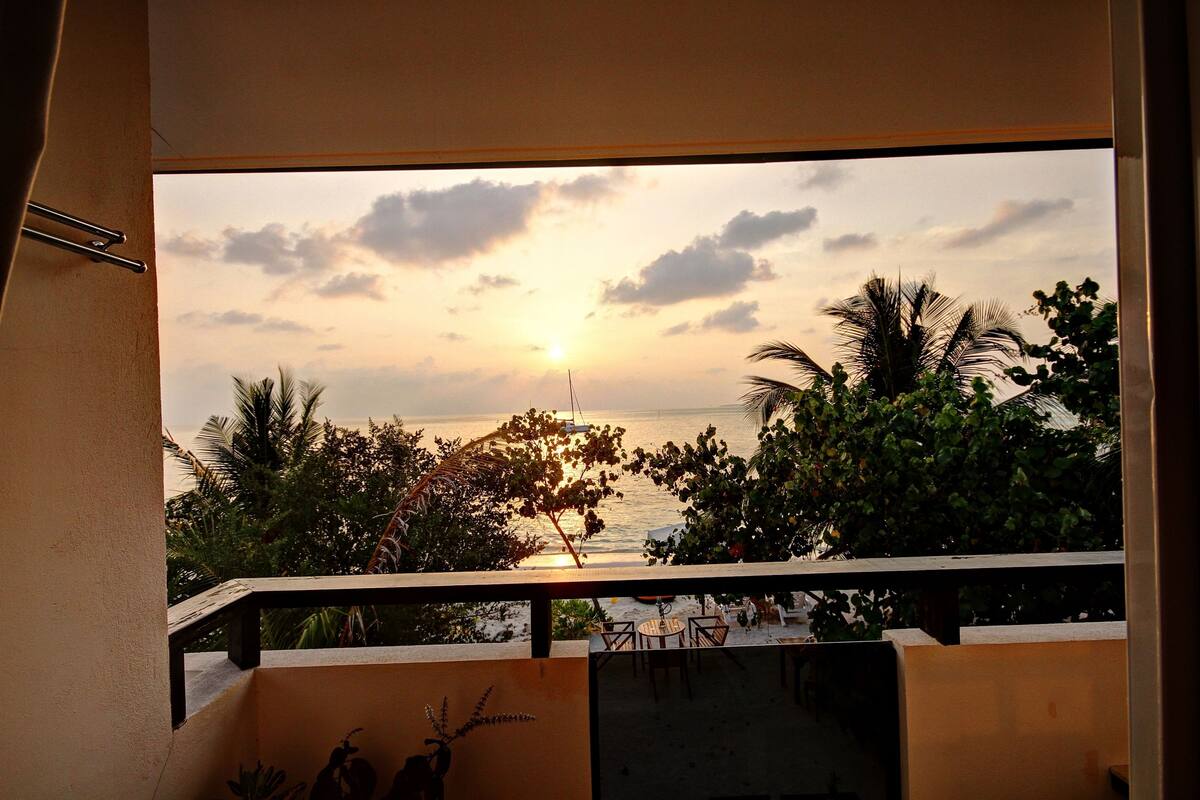 Un balcon offrant une vue sur le coucher de soleil sur la mer, entouré de verdure.