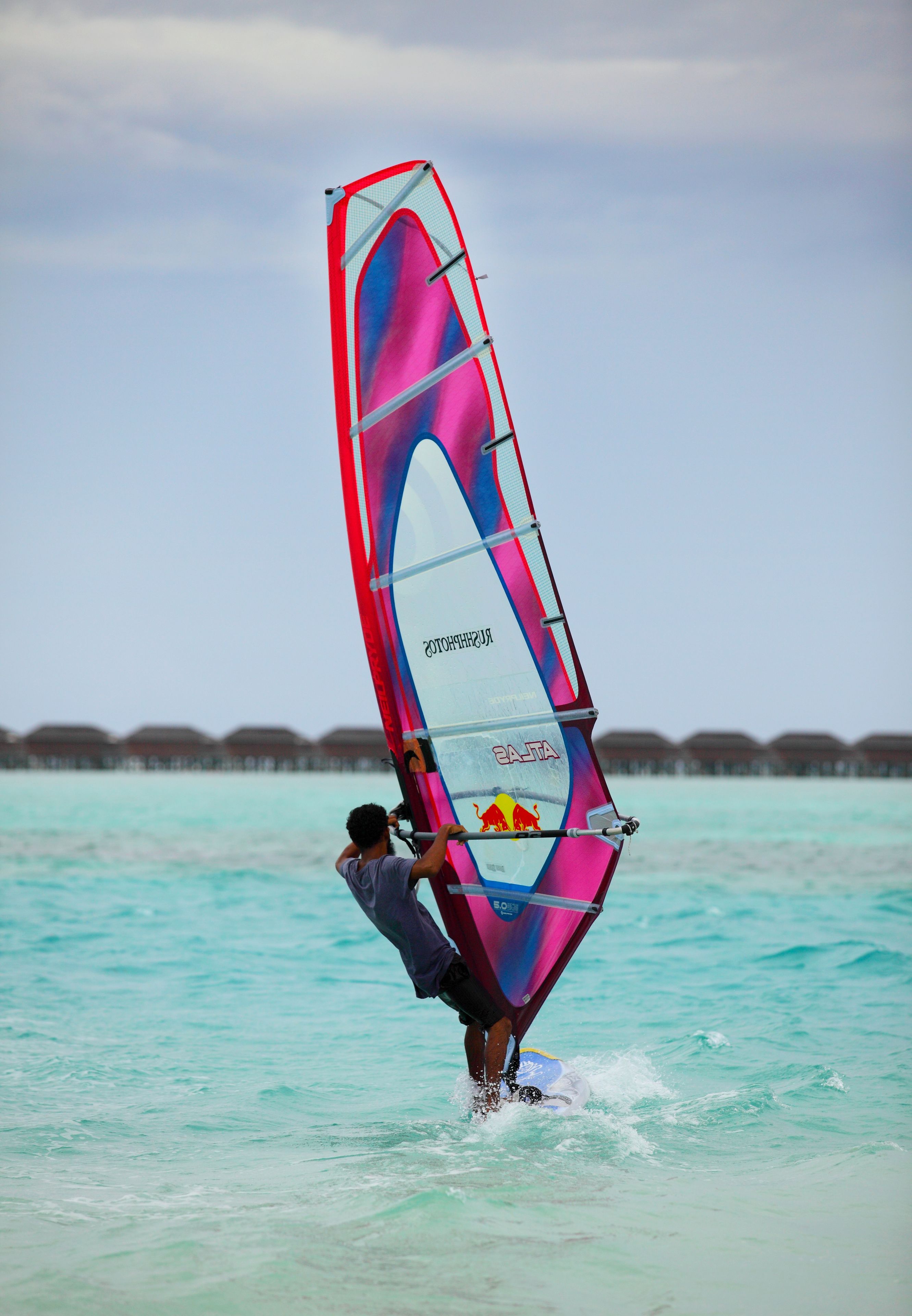 Una persona practicando windsurf en aguas turquesas con una vela colorida.