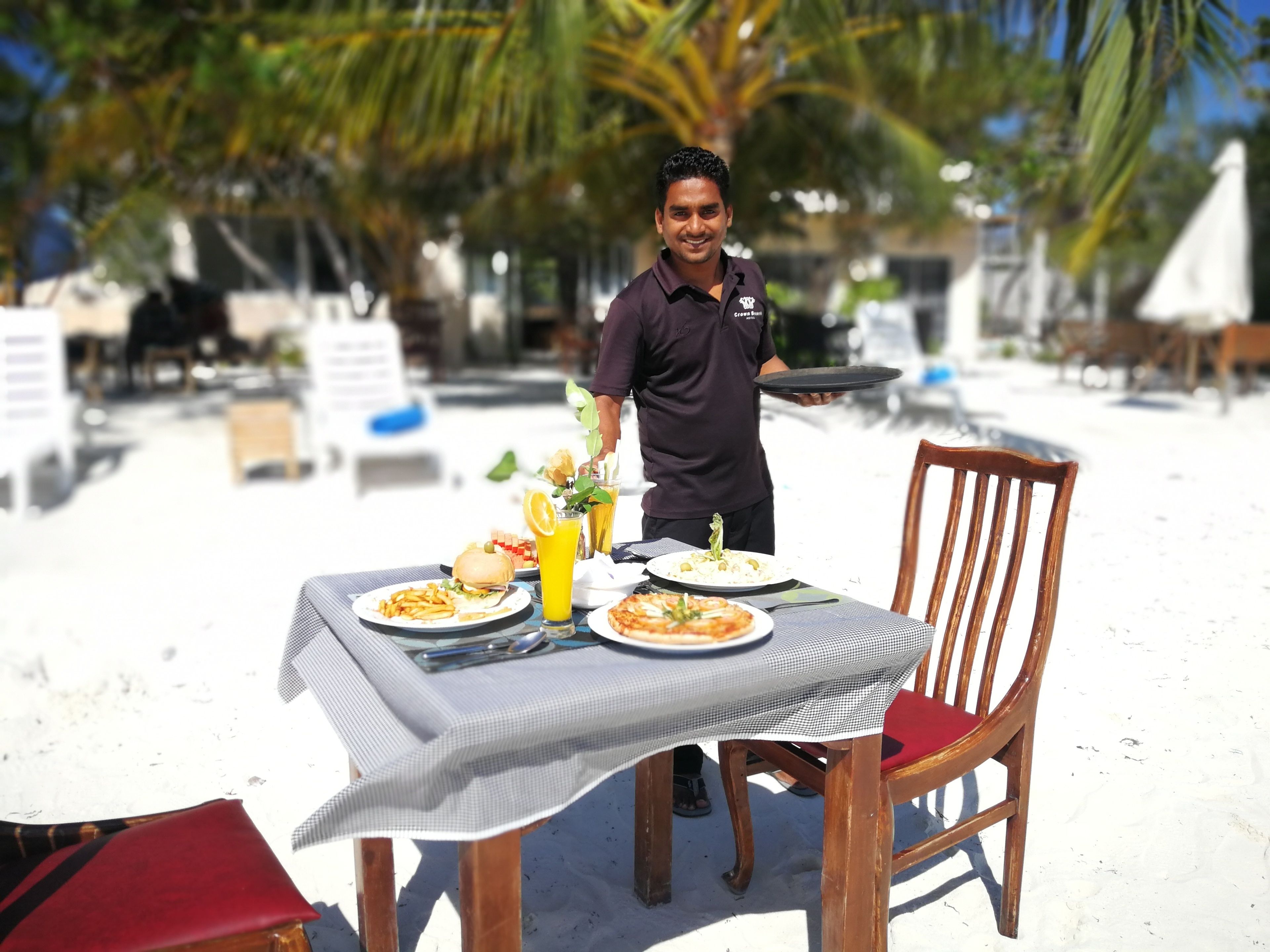 A table set with plates of food, a drink, and a waiter holding a tray.