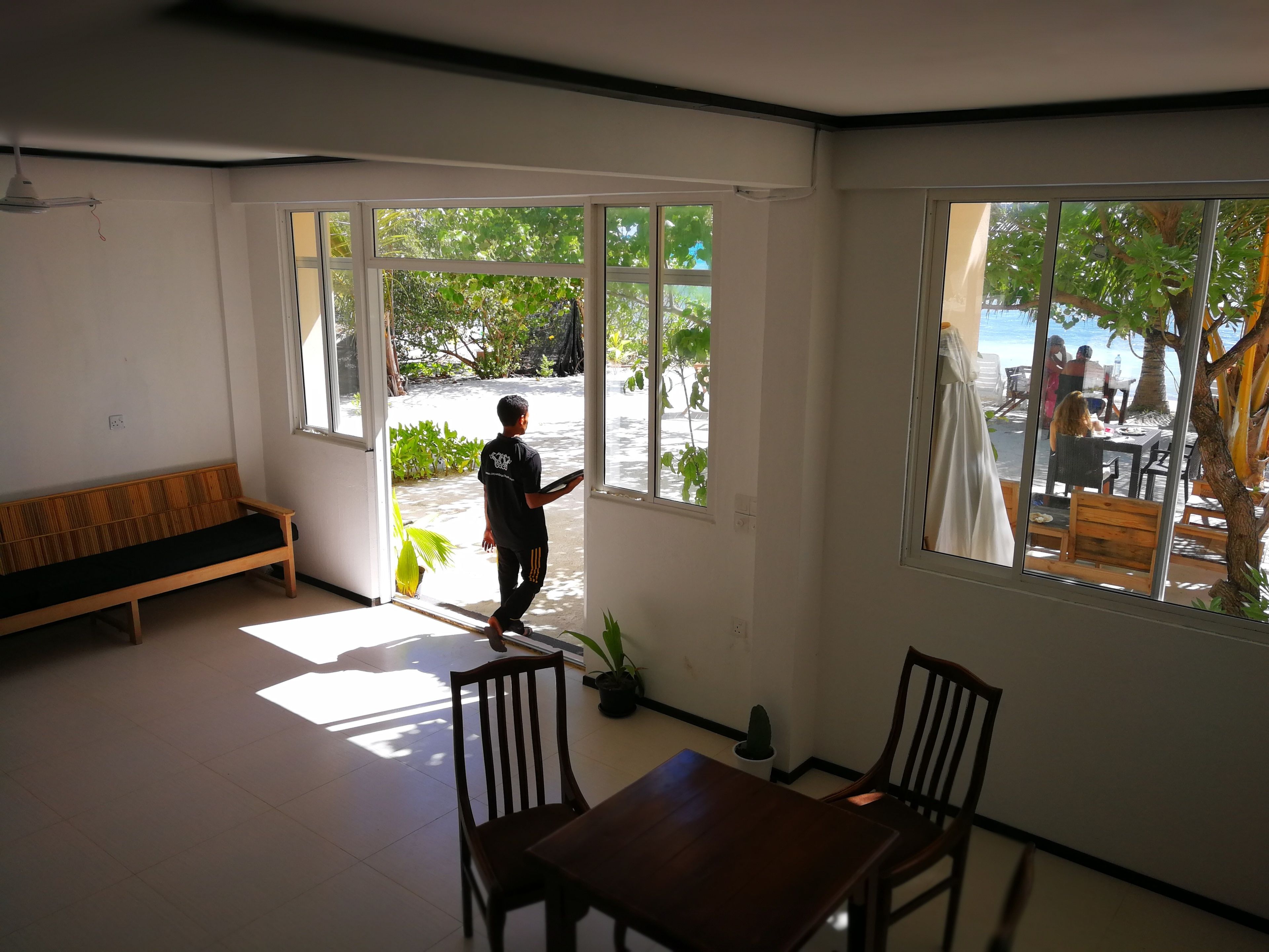 Ein Zimmer mit einer Holzbank, einem Esstisch mit Stühlen und großen Fenstern mit Blick auf einen Strand und Palmen.