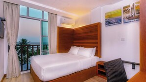 A hotel room with a large bed, a wooden headboard, a desk with a chair, and a balcony with a view of the sea. - Express Inn (Hulhumalé)
