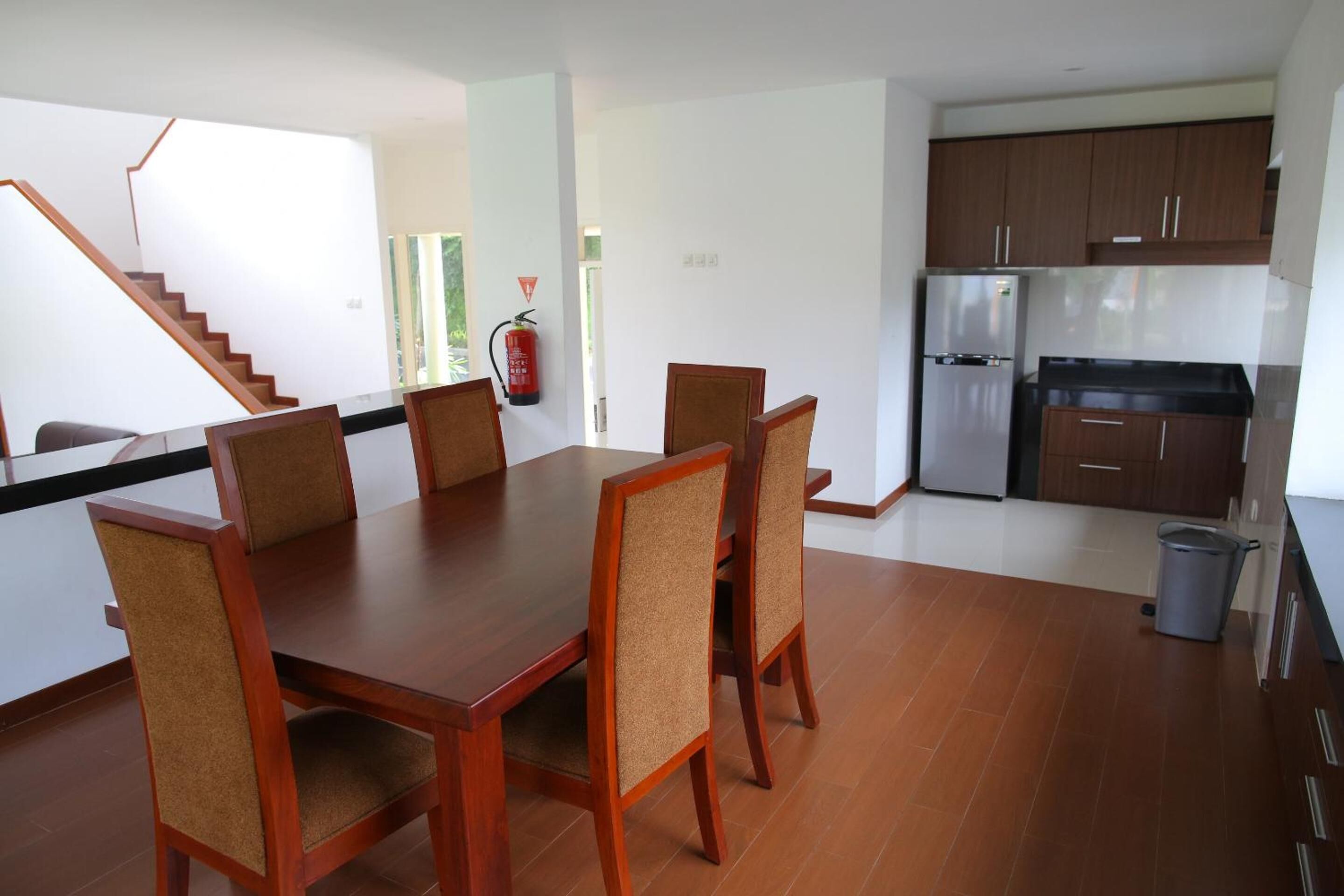 A modern kitchen with wooden cabinets, a stainless steel refrigerator, and a dining area with a wooden table and chairs.
