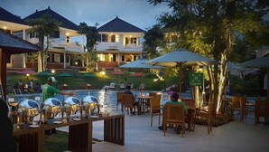 An outdoor pool area with lounge chairs and umbrellas, surrounded by buildings with a tropical setting. - Samara Resort (Batu)