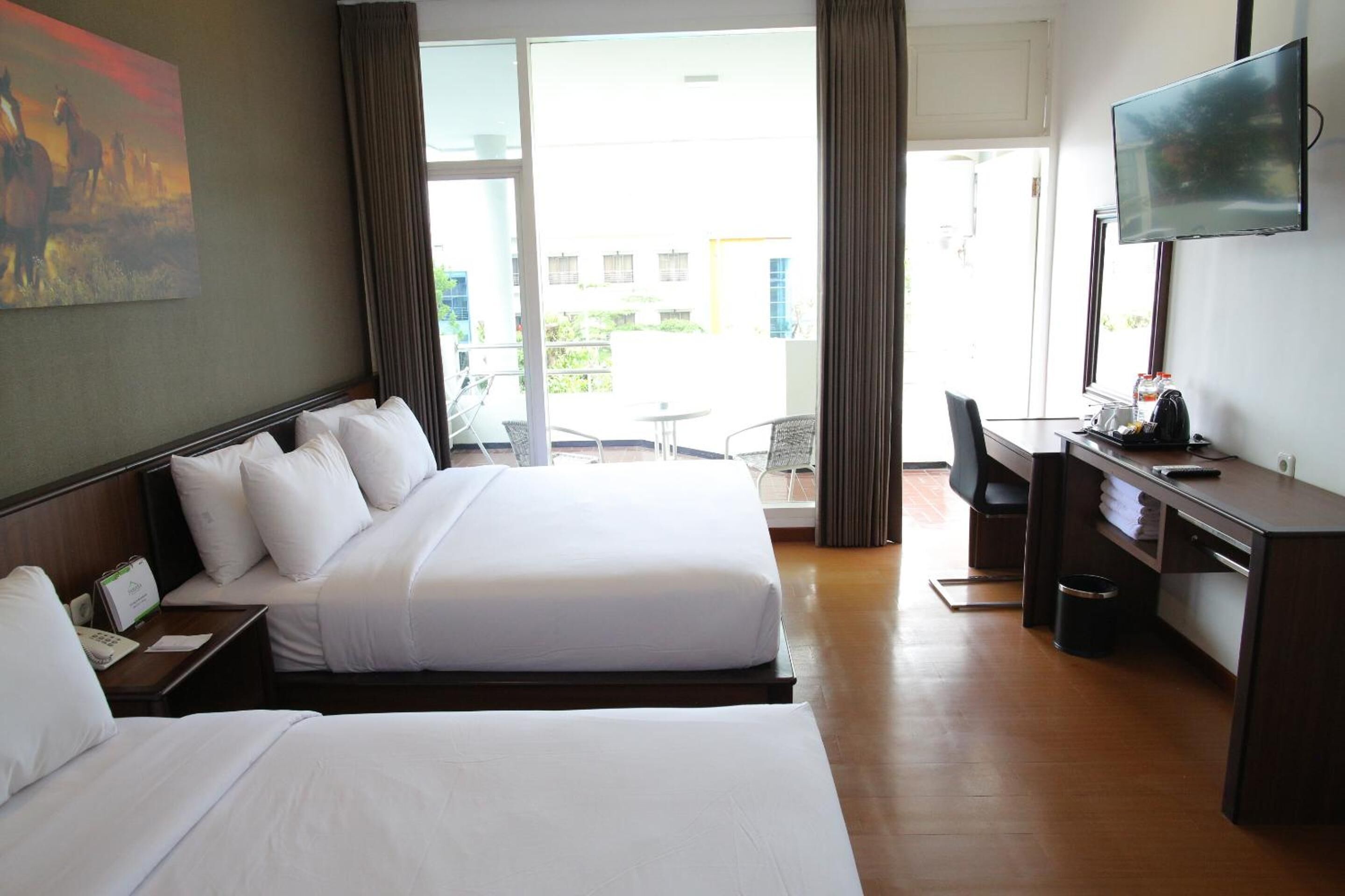A hotel room with two beds, a desk, a TV, and a view of the outside.