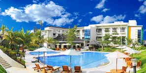 A resort with a swimming pool, lounge chairs, umbrellas, and a building with multiple floors and balconies.
